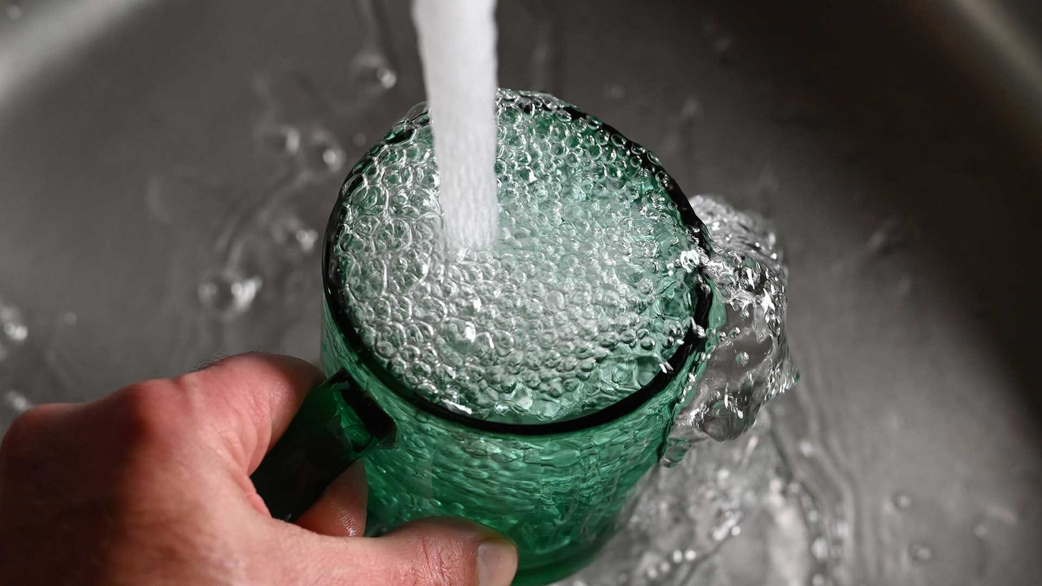 Grünes Glas wird mit Wasser aus dem Wasserhahn gefüllt
