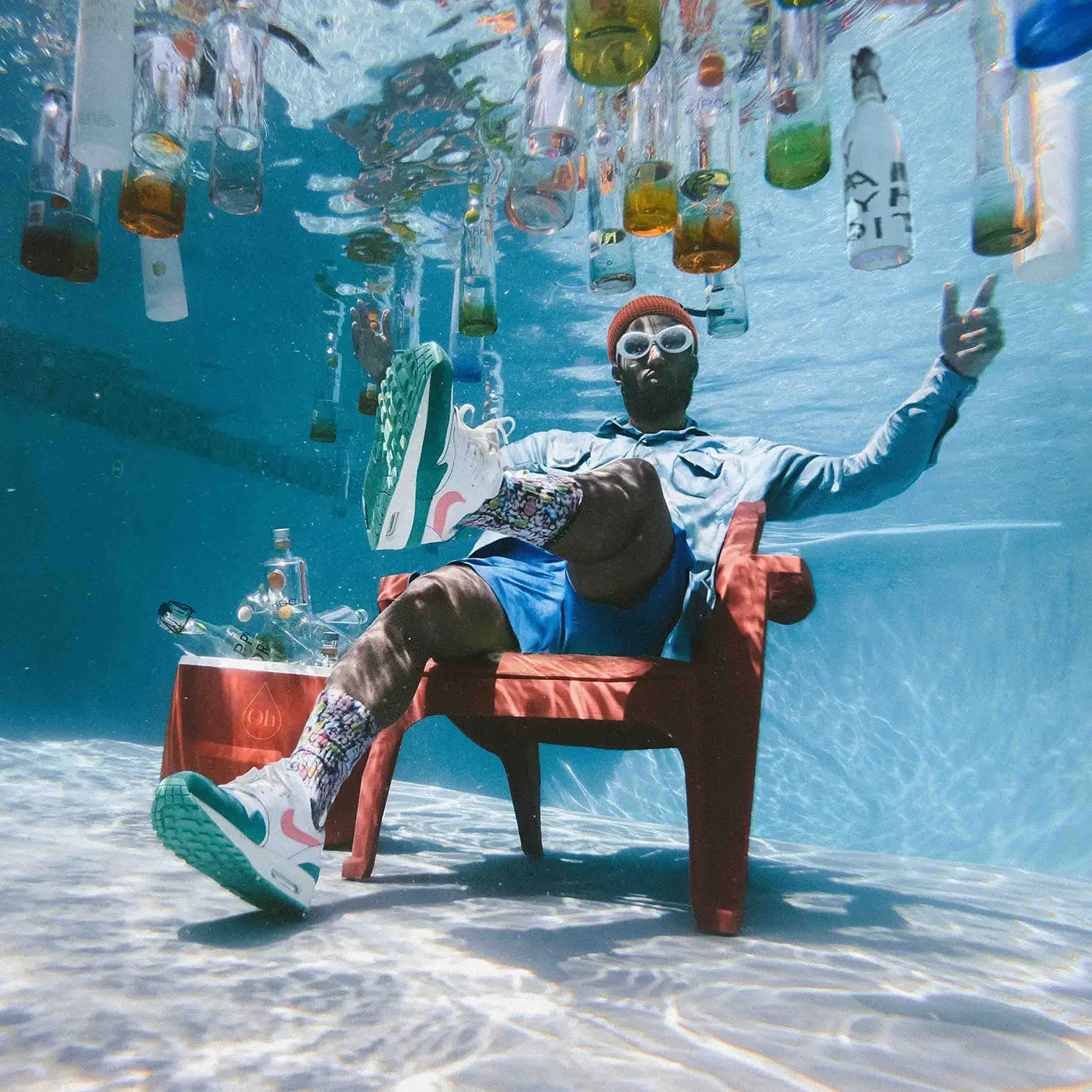 Mann sitzt unter Wasser im Pool, um ihn herum schwimmenden Wasserflaschen