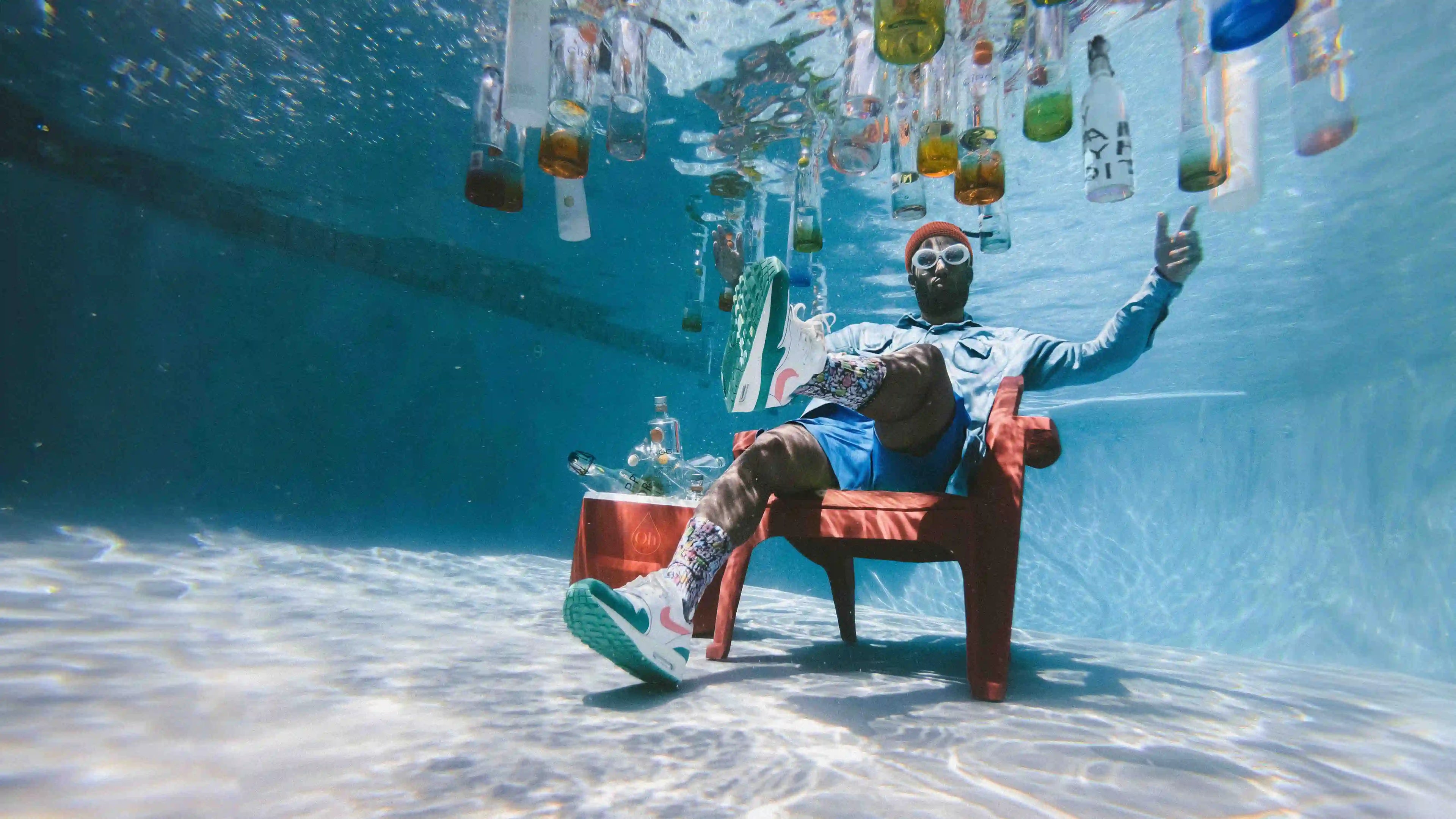 Mann sitzt unter Wasser im Pool mit schwimmenden Wasserflaschen